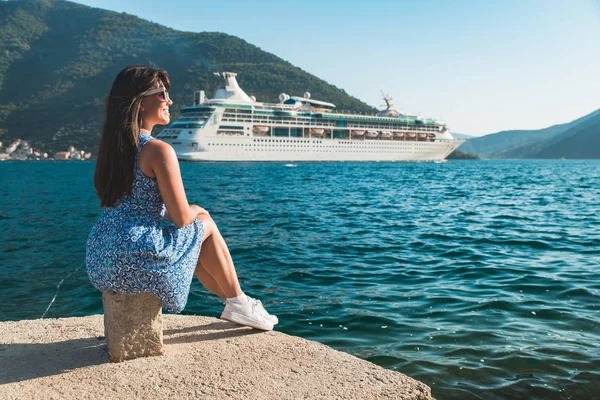 Joven bonita mujer sentado en muelle mirando al mar con crucero — Foto de Stock