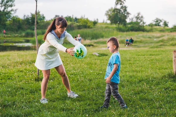 Mutter spielt mit Sohn im Ball auf der grünen Wiese. — Stockfoto