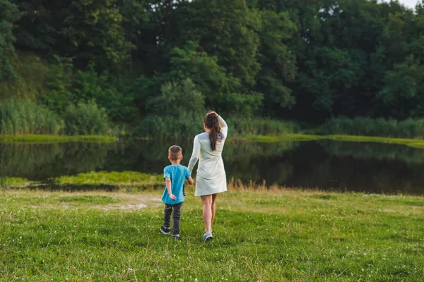 Мати з дитиною тримає руки йде до озера — стокове фото