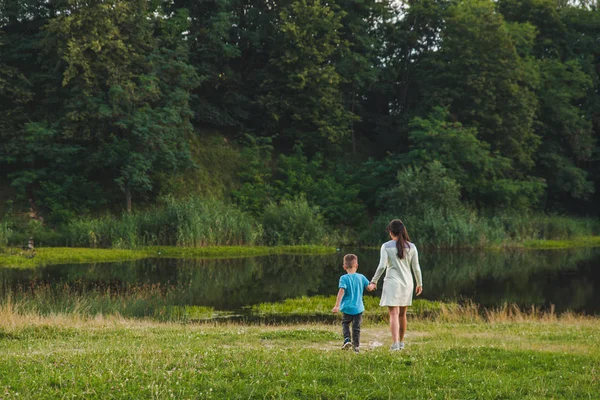 Madre con el niño cogido de la mano caminando al lago —  Fotos de Stock