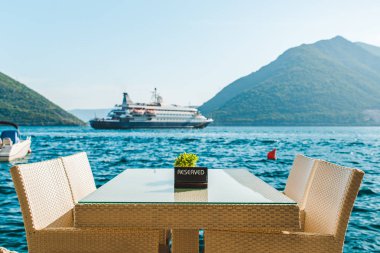 güzel bir deniz ve dağ manzarası ile sahilde Cafe tablo. üzerinde ayrılmış plaka. Cruise liner arka plan üzerinde
