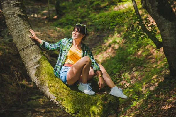 Woman sitting no tree in forest. sun is shining on face — Stock Photo, Image