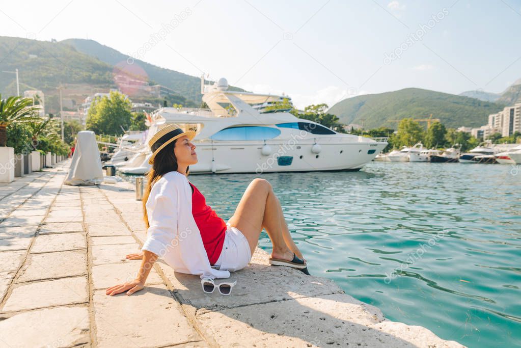 woman sitting at seashore in harbor with beautiful view of yachts and mountains
