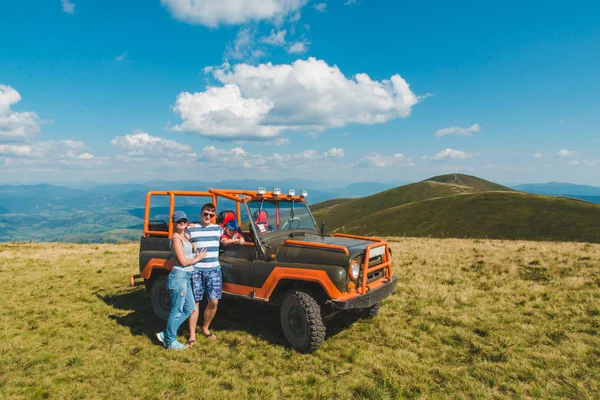 Giovane famiglia in posa vicino suv auto con bella vista sulle montagne — Foto Stock