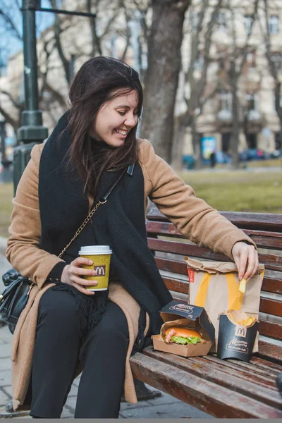 Львов, Украина - 28 февраля 2019 года: женщина ест фаст-фуд на городской скамейке — стоковое фото