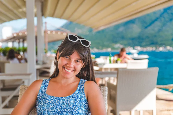 Giovane bella donna seduta in un caffè in riva al mare con le montagne sullo sfondo — Foto Stock