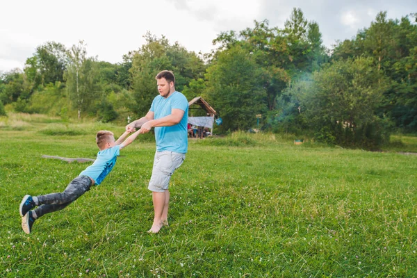 Mann spinnt Jungen auf der grünen Wiese. Herumspielen — Stockfoto