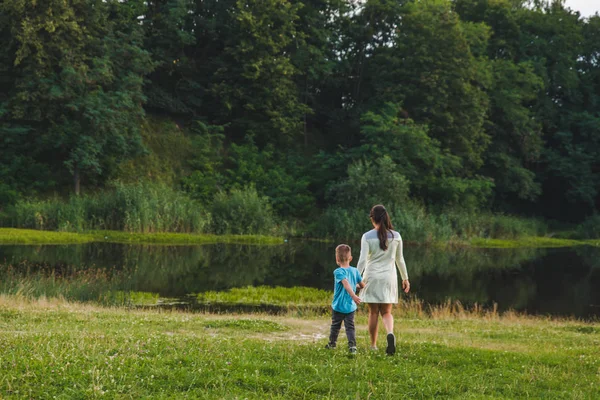 Madre con bambino che si tiene per mano camminando verso il lago — Foto Stock