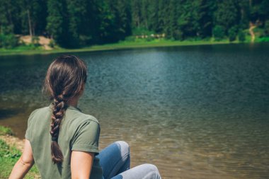 Ukrayna Karpat dağlarında dağ gölü Plajı'nda oturan genç yetişkin kadın