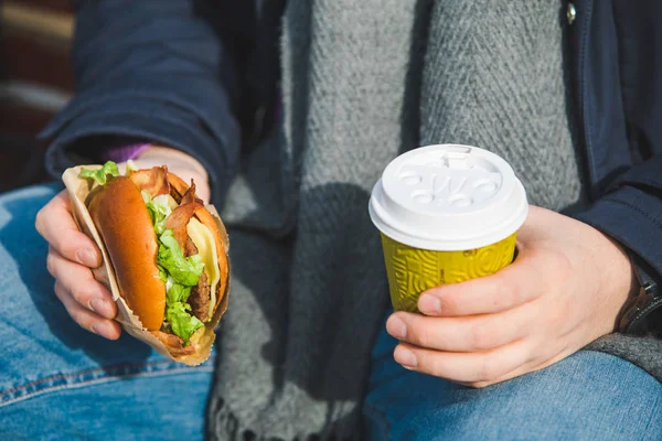 Man handen close-up houden hamburger met koffiekopje — Stockfoto