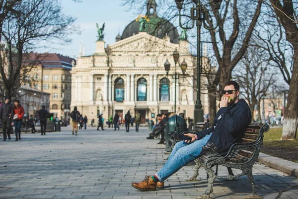 Ember eszik hamburgert szörfözés internet telefon ül a padon — Stock Fotó