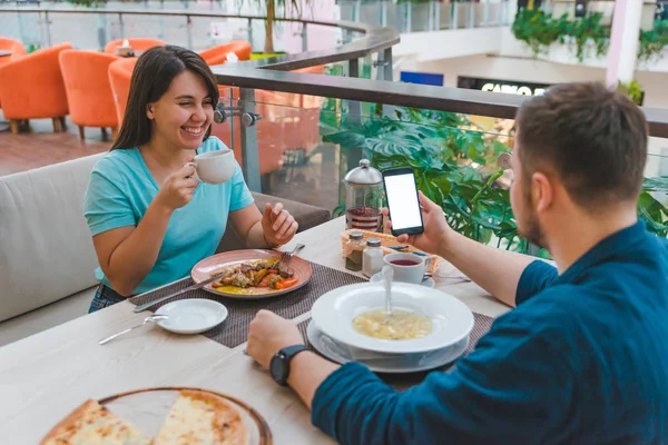 Couple eating in cafe. man show phone screen. white copy space — Stock Photo, Image