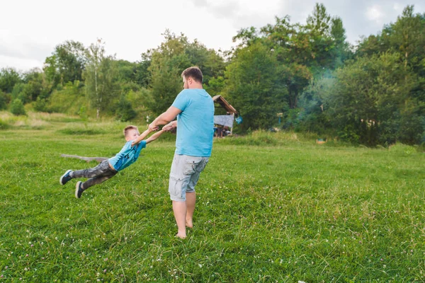 Человек крутящийся мальчик на зеленом поле. играя вокруг — стоковое фото