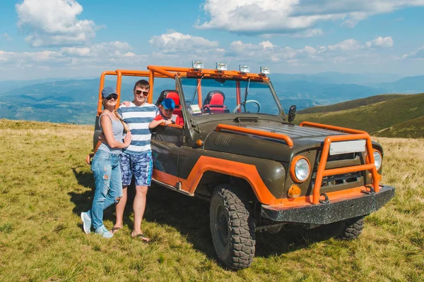 Giovane famiglia in posa vicino suv auto con bella vista sulle montagne — Foto Stock