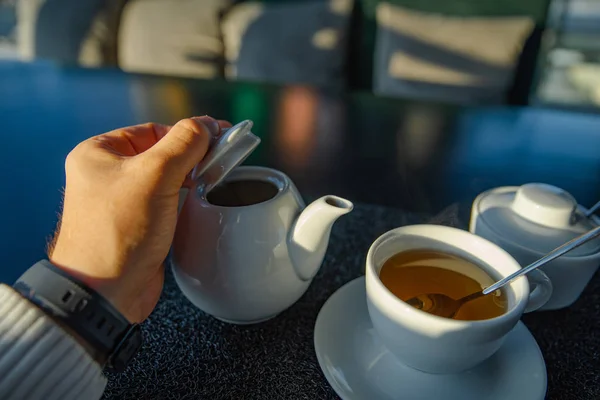 Hombre mano sosteniendo taza con té. hervidor de agua sobre fondo —  Fotos de Stock