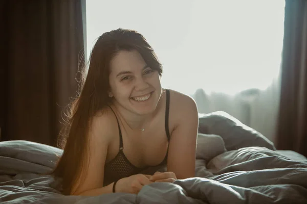 Молодая красивая женщина в черном лифчике сидит на кровати. утреннее время — стоковое фото