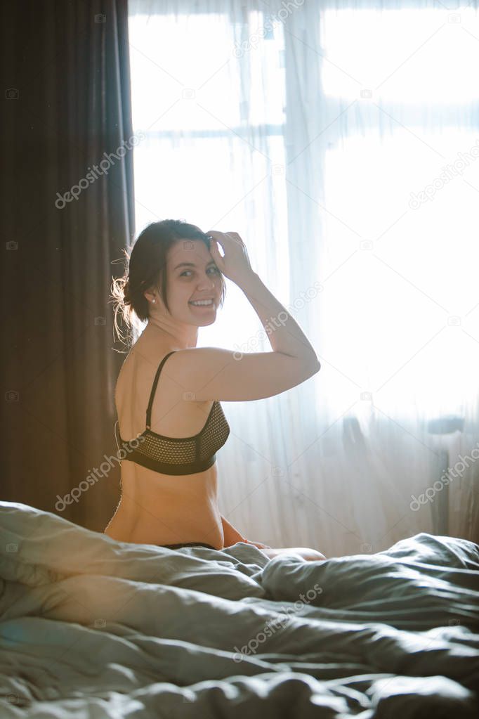 young pretty woman in black bra sitting on bed. morning time