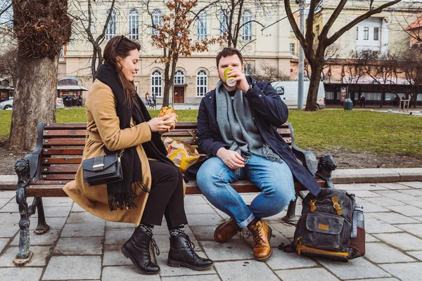 Young adult couple eating fast food on bench of city park — Stock Photo, Image