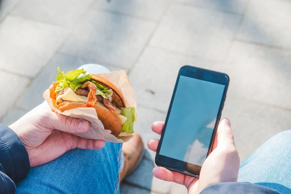 Man holding burger and mobile phone. white screen — Stock Photo, Image