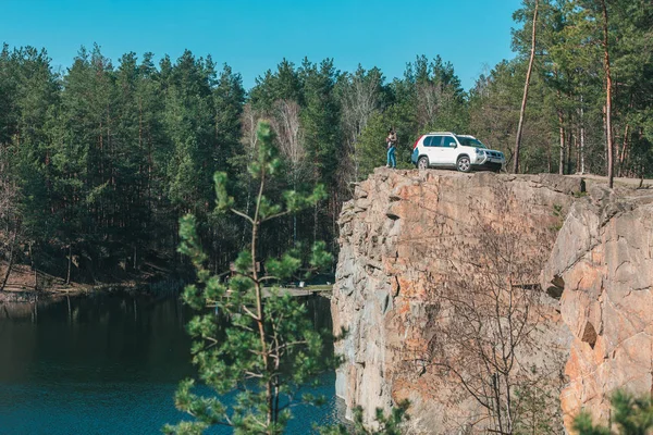 Mladý muž na hraně s nádherným výhledem na jezero u bílého vozu SUV — Stock fotografie