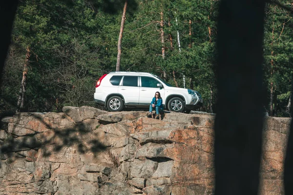 Frau sitzt auf Klippe mit schöner Aussicht bei sonnigem Tag. Geländewagen im Hintergrund — Stockfoto