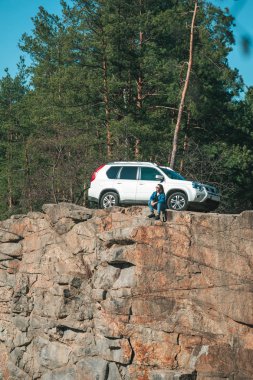 kadın güneşli bir gün güzel görünümü ile uçurumun üzerinde oturuyor. arka planda SUV araba