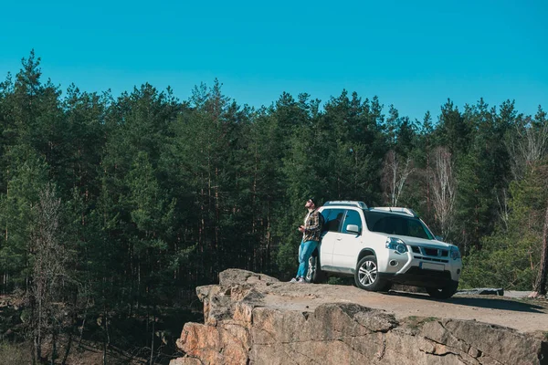 Joven en el borde con hermosa vista del lago cerca de coche suv blanco — Foto de Stock