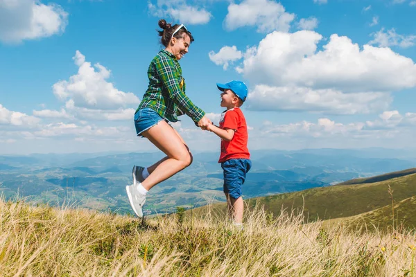 Madre con hijo saltando en la cima de la montaña. hermosa vista del paisaje —  Fotos de Stock