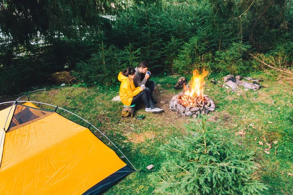 Couple sitting near campfire drinking tea. yellow tent — Stock Photo, Image