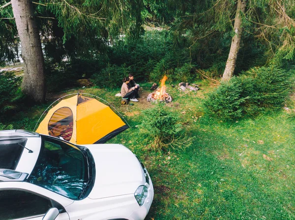 Paar sitzt am Lagerfeuer und trinkt Tee. Gelbes Zelt und weißer Geländewagen — Stockfoto