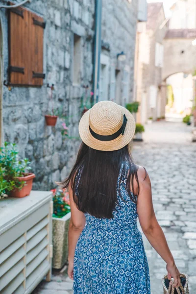 Woman walking by small perast streets in hat and blue dress — Stockfoto