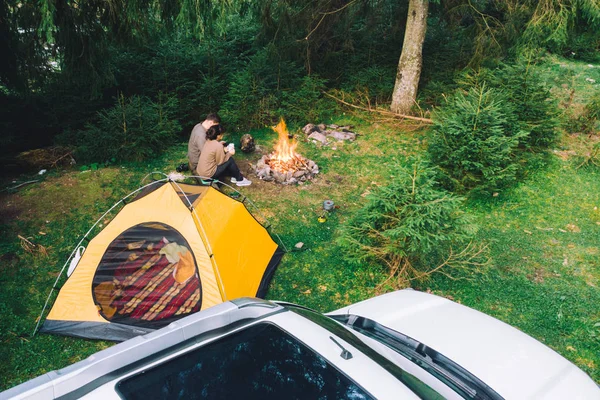 Paar sitzt am Lagerfeuer und trinkt Tee. Gelbes Zelt und weißer Geländewagen — Stockfoto