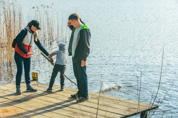 Padre y madre con niño jugando con el banco cerca del agua —  Fotos de Stock