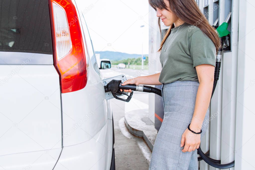 young pretty woman at gas station filling up car tank