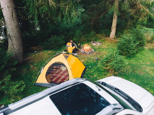 Paret sitter nära lägerelden dricka te. gula tält och vit suv bil — Stockfoto
