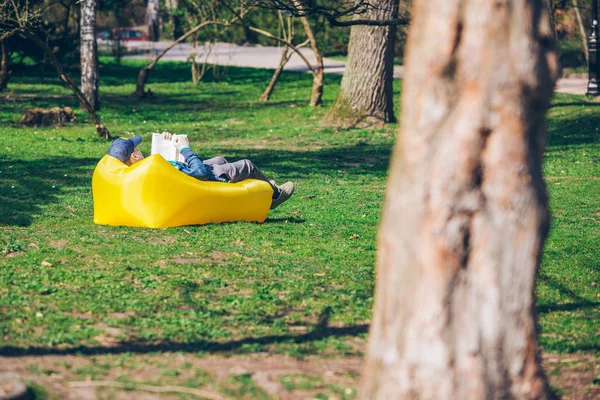 Concepto de lectura de libros. hombre en parque de la ciudad en colchón inflable — Foto de Stock