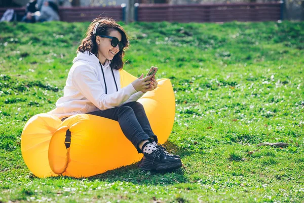 Jovem mulher bonita no colchão inflável amarelo no parque da cidade surfando no telefone — Fotografia de Stock