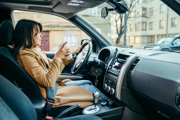 Jonge mooie vrouw rijdt auto onder het genot van kopje koffie — Stockfoto