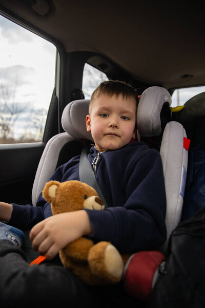 cute little boy with fluffy bear in car chair at back seats in road trip.