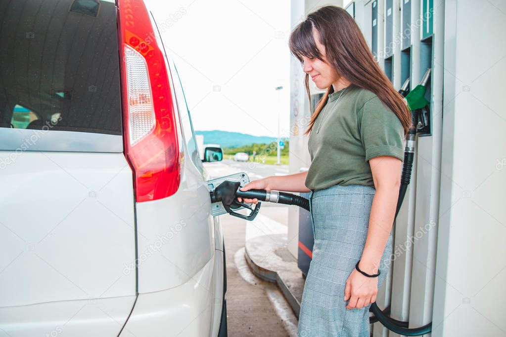 young pretty woman at gas station filling up car tank