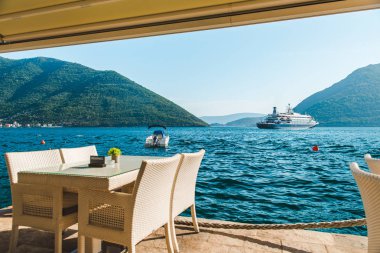 güzel bir deniz ve dağ manzarası ile sahilde Cafe tablo. üzerinde ayrılmış plaka. Cruise liner arka plan üzerinde