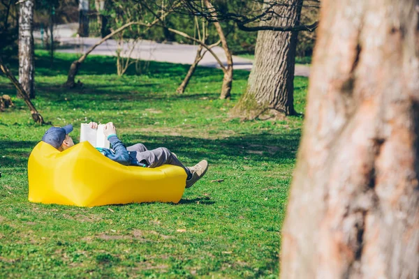 Concepto de lectura de libros. hombre en parque de la ciudad en colchón inflable — Foto de Stock