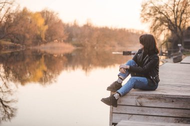 Gün batımında iskelede oturan genç ve güzel nehir manzaralı güzel bir kadın.
