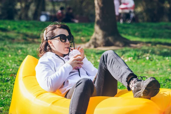 Woman drinking smoothie in city park laying on yellow inflatable mattress — 스톡 사진