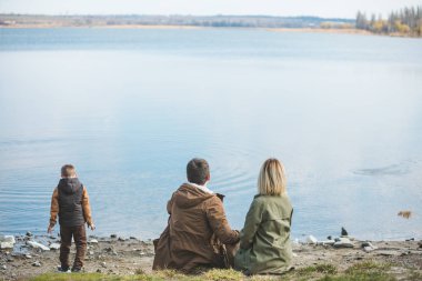 su kenarında yürüyen bir aile. Sahilde oturuyor. küçük çocuk suya taş atma