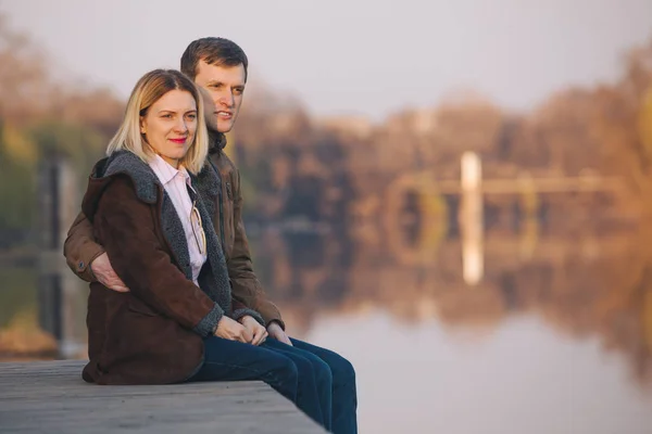 Couple mignon assis au bord de la rivière sur le coucher du soleil dans la chaude soirée d'automne — Photo