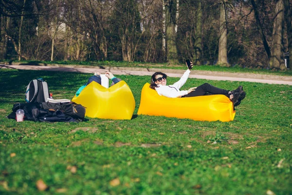 Pareja que pone en colchón inflable amarillo en el parque de la ciudad. libro de lectura. tomar selfie — Foto de Stock