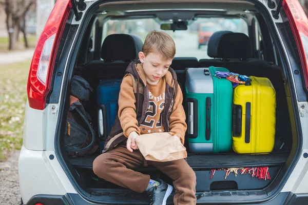 Little kid looking into paper bag with candies sitting in car trunk — Stock Photo, Image