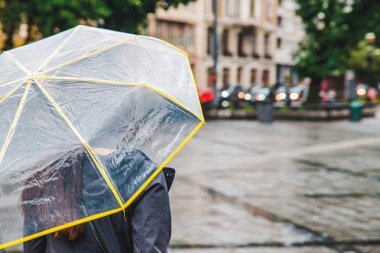 woman walking by wet rainy streets under transparent umbrella