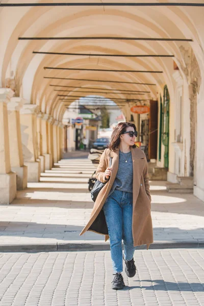Молодая довольно модная женщина, идущая в коричневом пальто по улице — стоковое фото